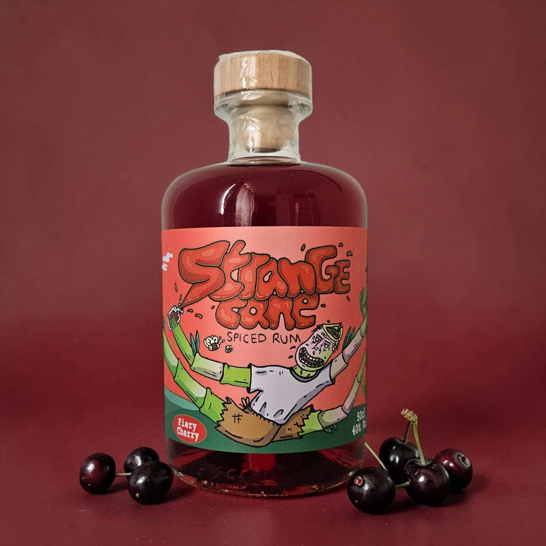 Strange Cane Fiery Cherry spiced rum bottle on a red background with fresh cherries