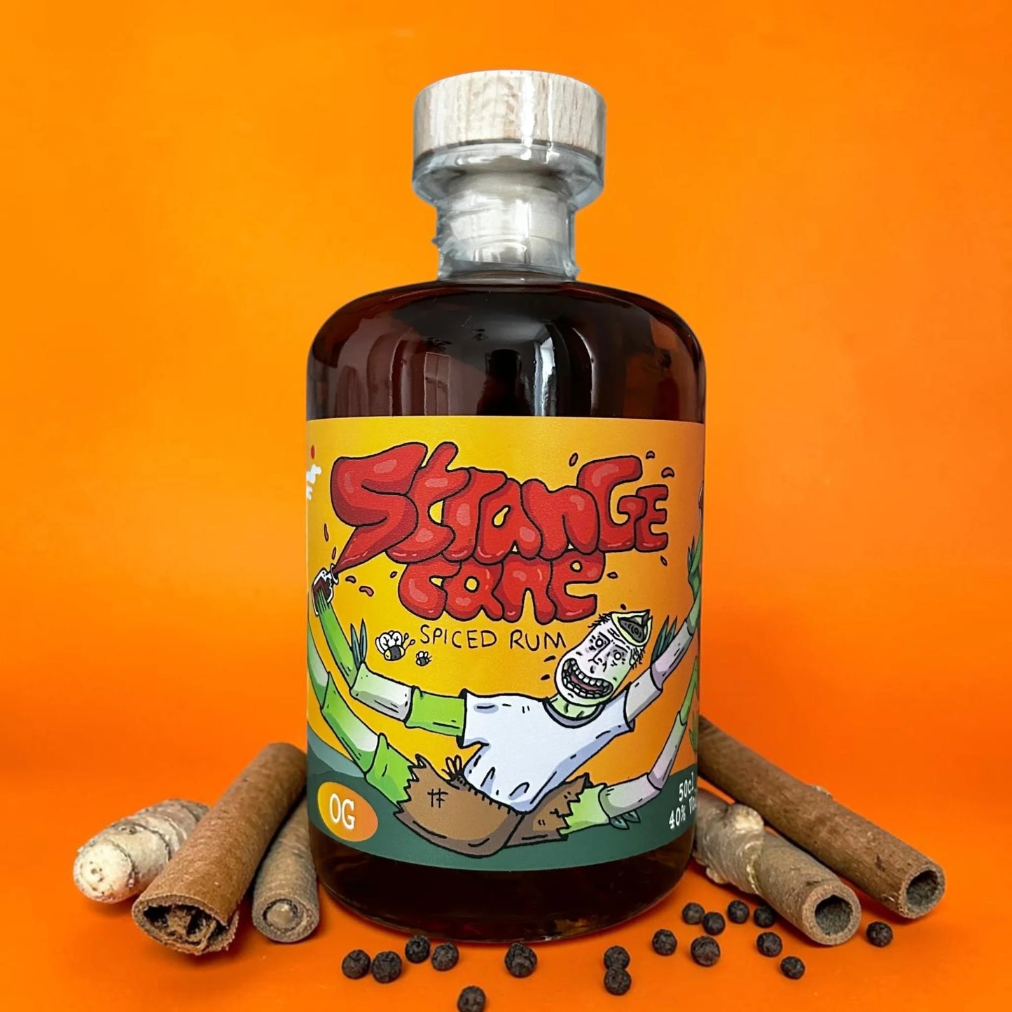 The OG Strange Cane spiced rum bottle on an orange background with ginger and cinnamon