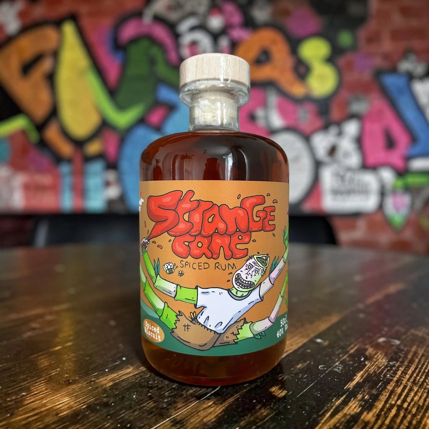Strange Cane Spiced Biscuit spiced rum on wooden table with graffiti wall